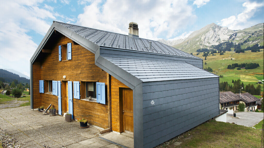 Casa di montagna in Svizzera con facciata in legno abbinata a tetto e scaglie per facciata PREFA in grigio pietra