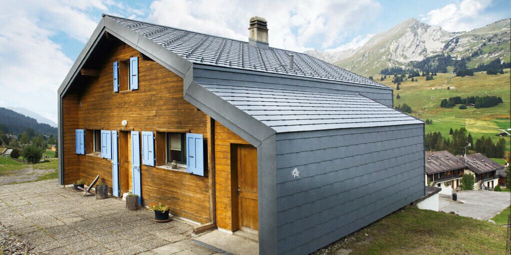 Haus in den Bergen der Schweiz mit Holzfassade kombiniert mit der PREFA Dach- und Wandraute in Steingrau