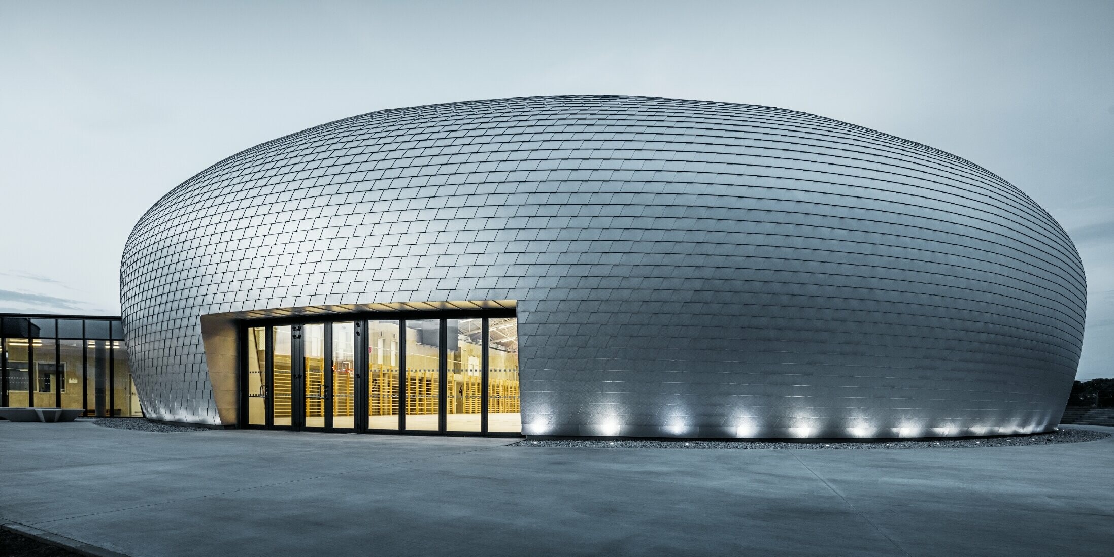 Sporthalle in Tschechien in Form eines UFOs verkleidet mit der PREFA Wandschindel in Naturblank bei Sonnenaufgang.