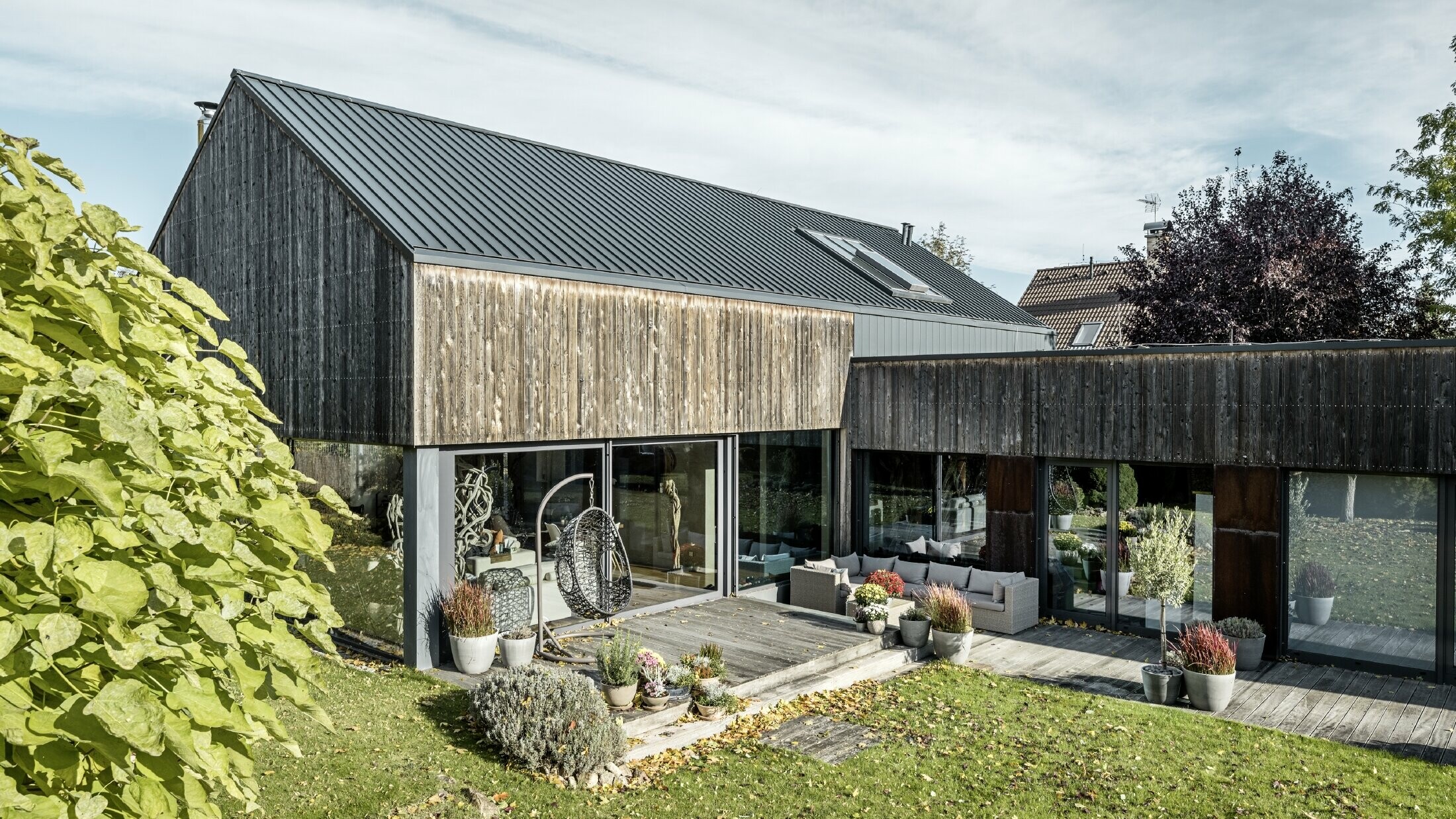 Casa unifamiliare con tetto a due falde, rivestito con aggraffatura doppia PREFALZ in antracite e facciata di legno invecchiata. Con una bella terrazza in legno e grandi finestre al piano terra.