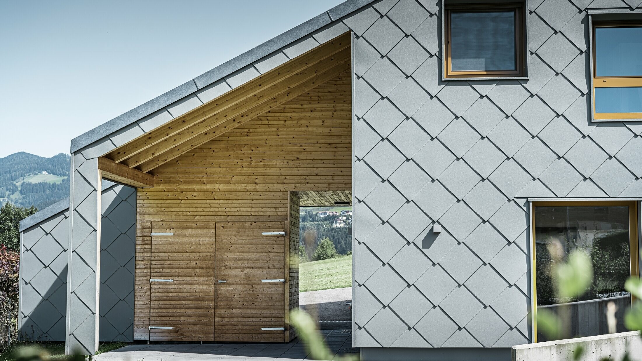 L'ingresso coperto è realizzato con un rivestimento orizzontale in legno, mentre il resto della facciata è rivestito con la scaglia per facciata PREFA grande in alluminio grigio chiaro.