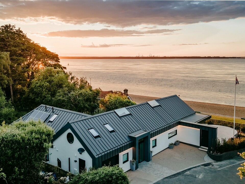 Ein luxuriöser Bungalow auf Isle of Wight, in der Nähe von Bournemouth, wurde mit PREFALZ in der Farbe P.10 Dunkelgrau eingedeckt und fügt sich harmonisch in natürliche Umgebung ein. Das moderne Gebäude mit der eleganten Aluminiumhülle, die mit einer weißen Putzfassade kombiniert wurde, vermittelt ein klares und unaufgeregtes Design. Das architektonische Highlight an der Südküste Englands liegt direkt am Meer. Im Hintergrund wird eine malerische Kulisse in der Golden Hour, der Stunde des Sonnenuntergangs, präsentiert.