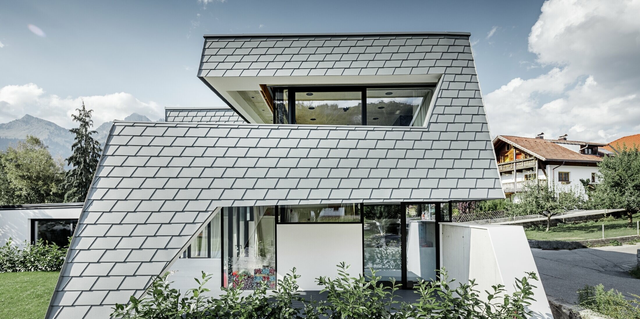 modernes Einfamilienhaus mit Flachdach, großen Fensterflächen und einer Schindel-Fassade in hellgrau aus Aluminium von PREFA