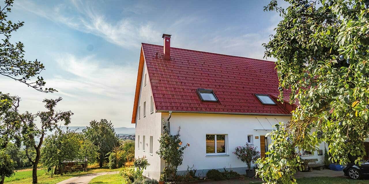 Casette romantiche in campagna con alberi e cespugli. Rivestite con un tetto PREFA in rosso ossido.