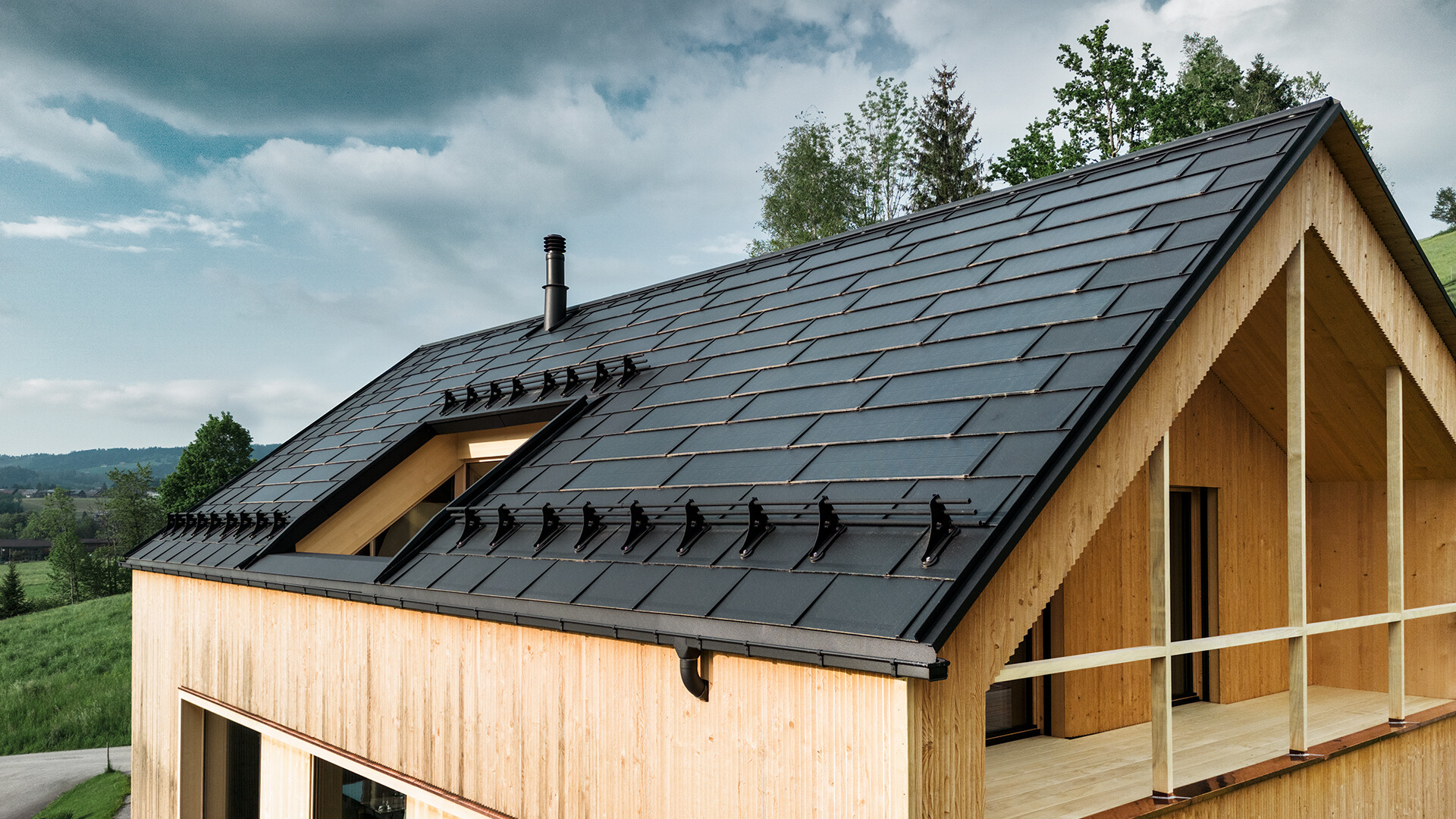 Pannello solare PREFA di colore nero su una casa ecologica a Egg, in Austria - durevole, efficiente dal punto di vista energetico ed esteticamente gradevole per l'architettura moderna. L'innovativa tegola fotovoltaica combina un tetto a prova di tempesta con un sistema fotovoltaico. I moduli fotovoltaici integrati si integrano armoniosamente nel tetto della casa indipendente.