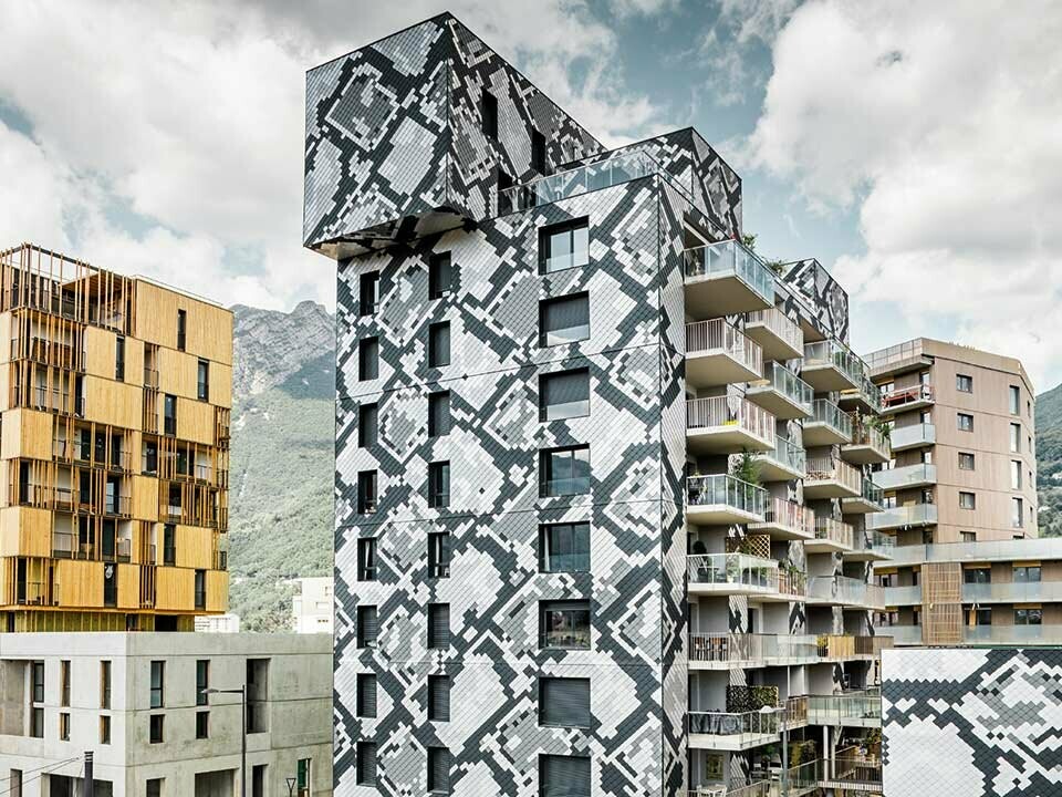 modernes und neues Wohnhaus in Grenoble, mit einer Aluminium Wandraute verkleidet, das Verlegemuster entspricht der Schlangenhaut einer Python in anthrazit, hellgrau, naturblank und silbermetallic, daneben ein Sandbrauner Wohnblock vor bewölktem Himmel