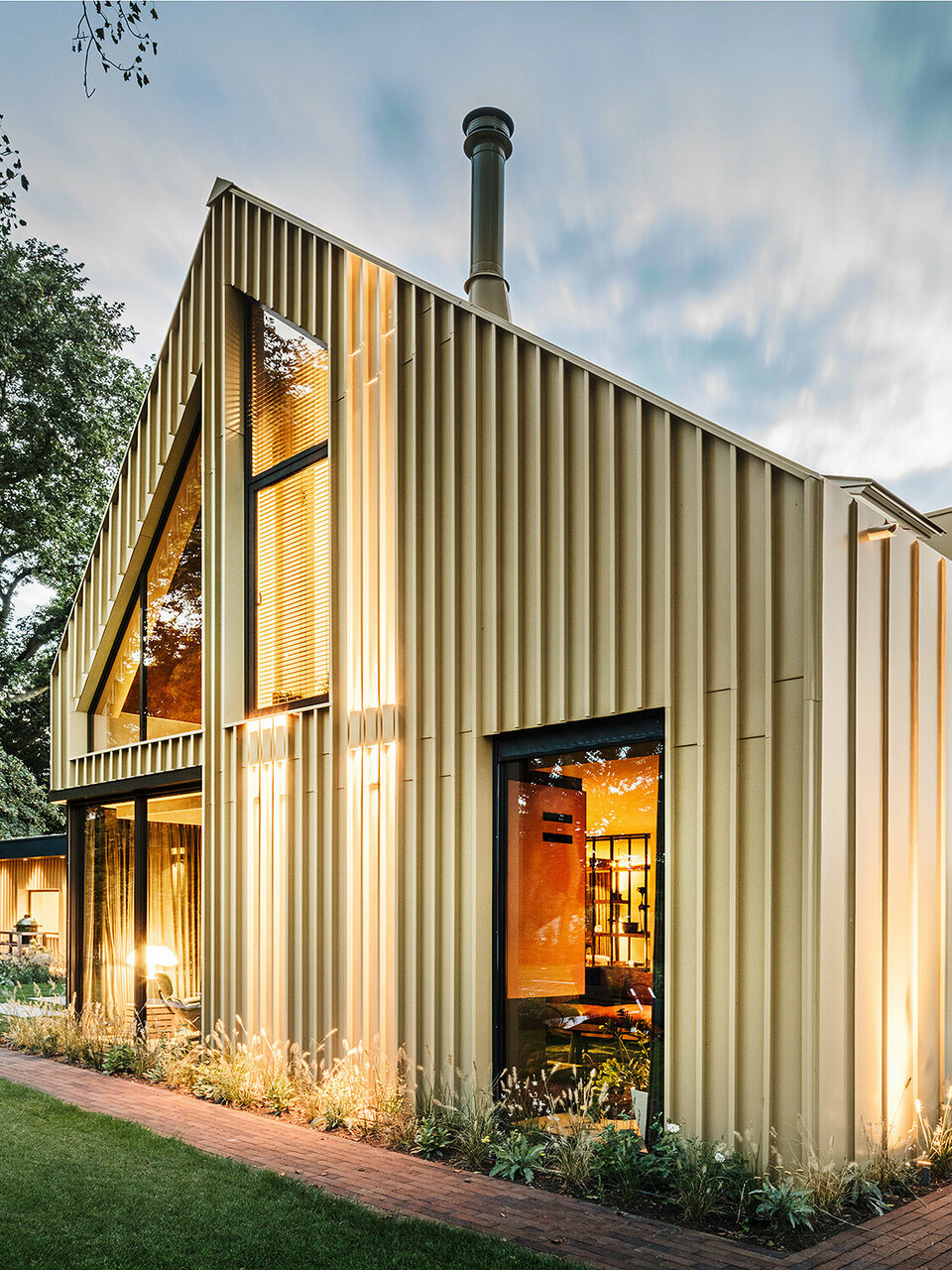 Abendaufnahme des Einfamilienhauses mit der linierten Aluminiumfassade und ausgeklügelten Außenbeleuchtung aus der seitlichen Normalperspektive.