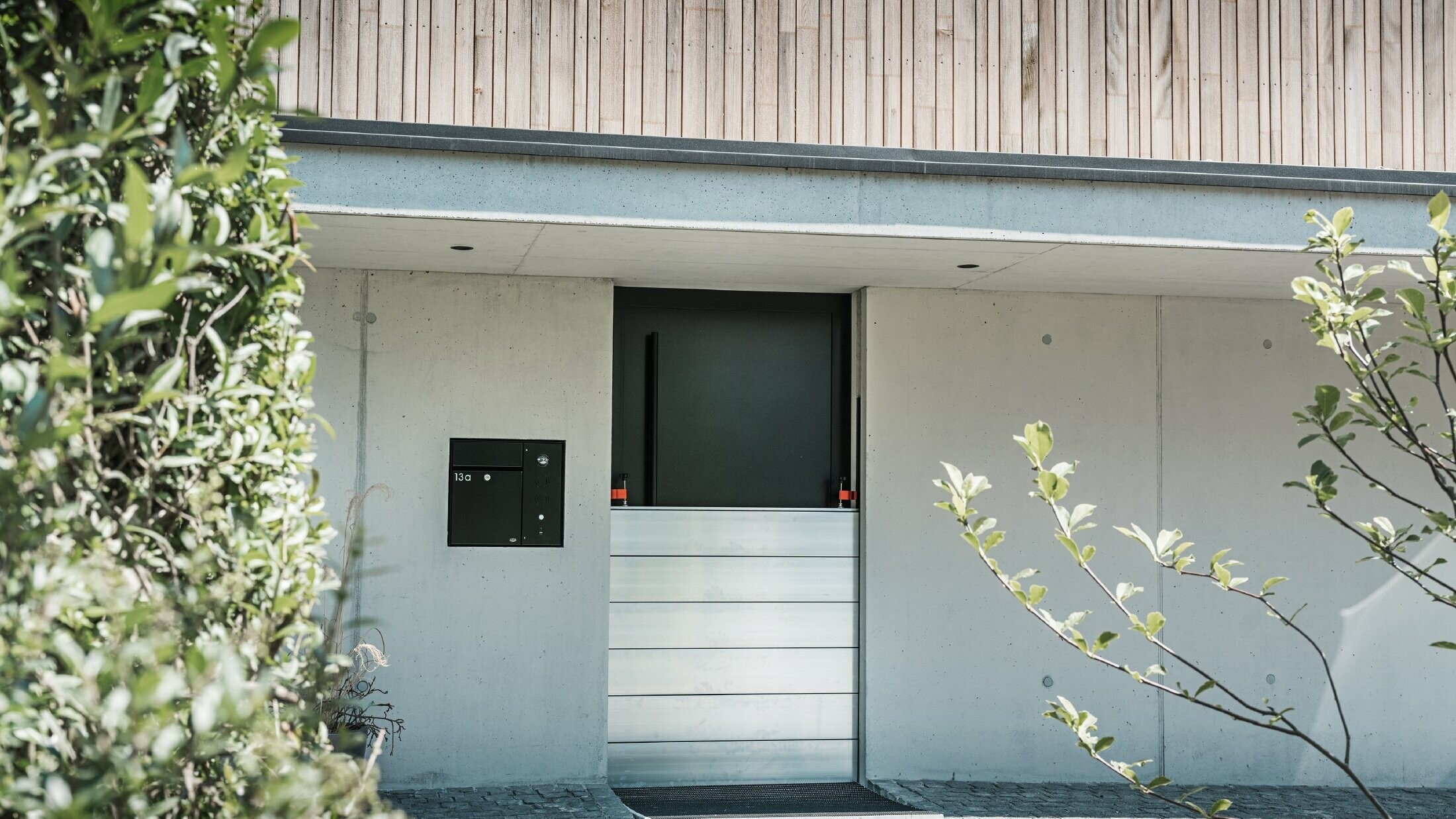 La protezione antiallagamento PREFA è installata davanti alla porta d'ingresso di una casa indipendente con facciata in legno. 