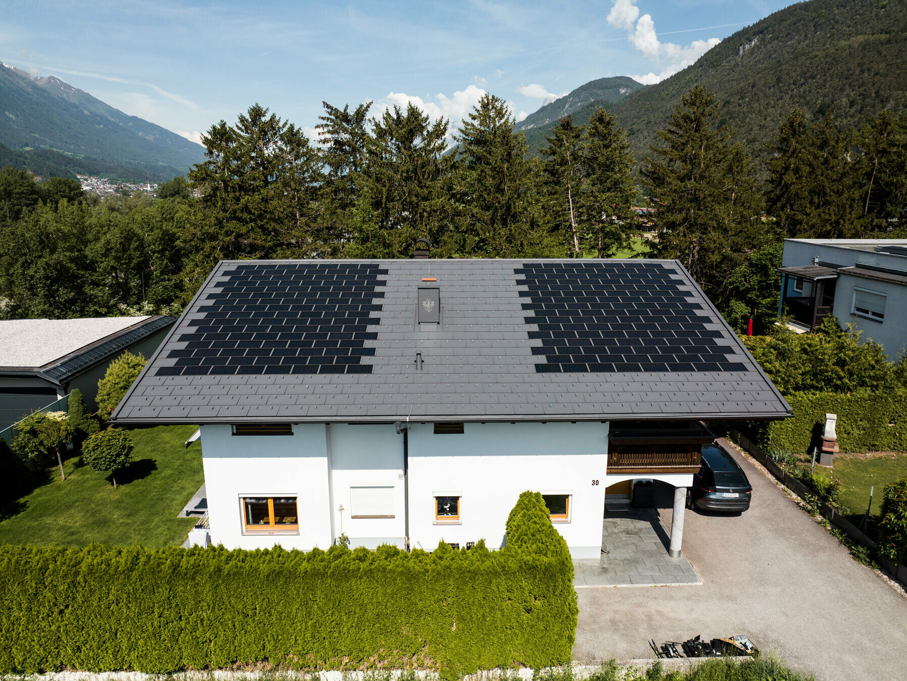 L'immagine mostra una casa unifamiliare coperta con la tegola fotovoltaica PREFA piccola e con la tegola R.16 nel colore P.10 grigio scuro in un ambiente rurale.