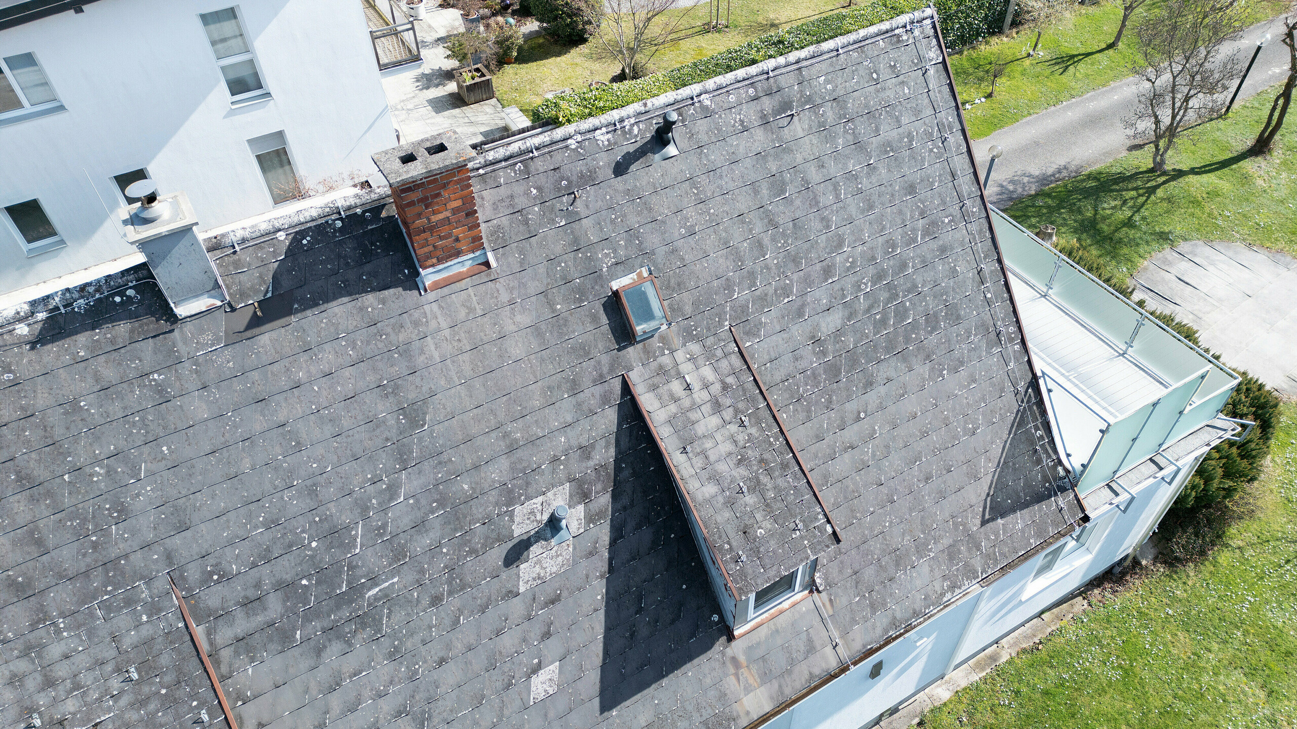 Dach eines Einfamilienhauses in Leonding vor der Sanierung mit PREFA Solardachplatten in Anthrazit. Nahaufnahme aus der Vogelperspektive, die den Zustand des alten, abgenutzten Eternit-Dachs mit sichtbaren Schäden zeigt. Die Notwendigkeit einer Dachsanierung und die Installation einer modernen, nachhaltigen Solaranlage wird deutlich. Dieses Bild veranschaulicht den Ausgangszustand vor der Umwandlung in eine energieeffiziente und wetterbeständige Dachkonstruktion.