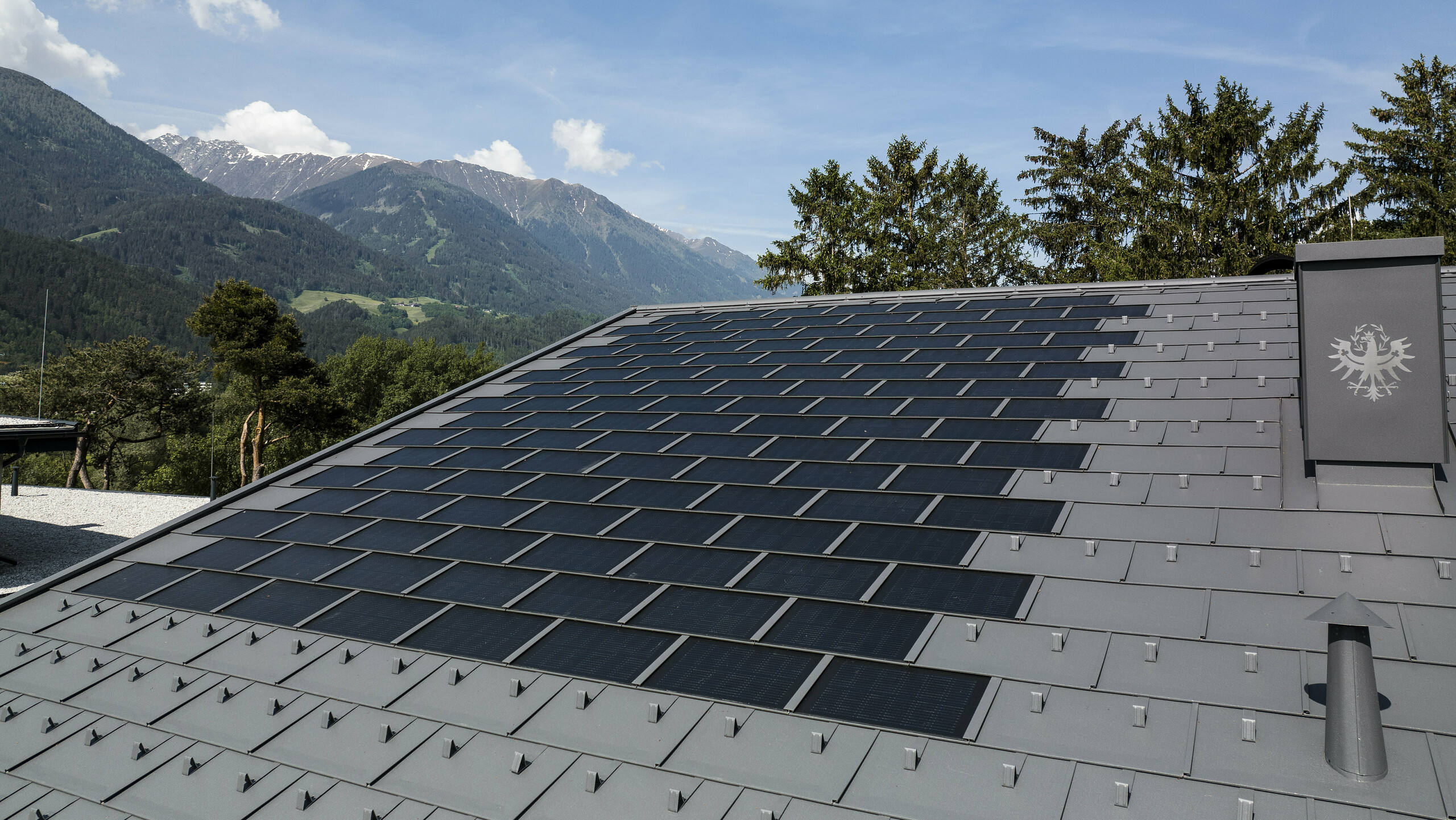 Una foto del tetto in Tirolo coperto con la tegola fotovoltaica PREFA R.16 nel colore P.10 grigio scuro.