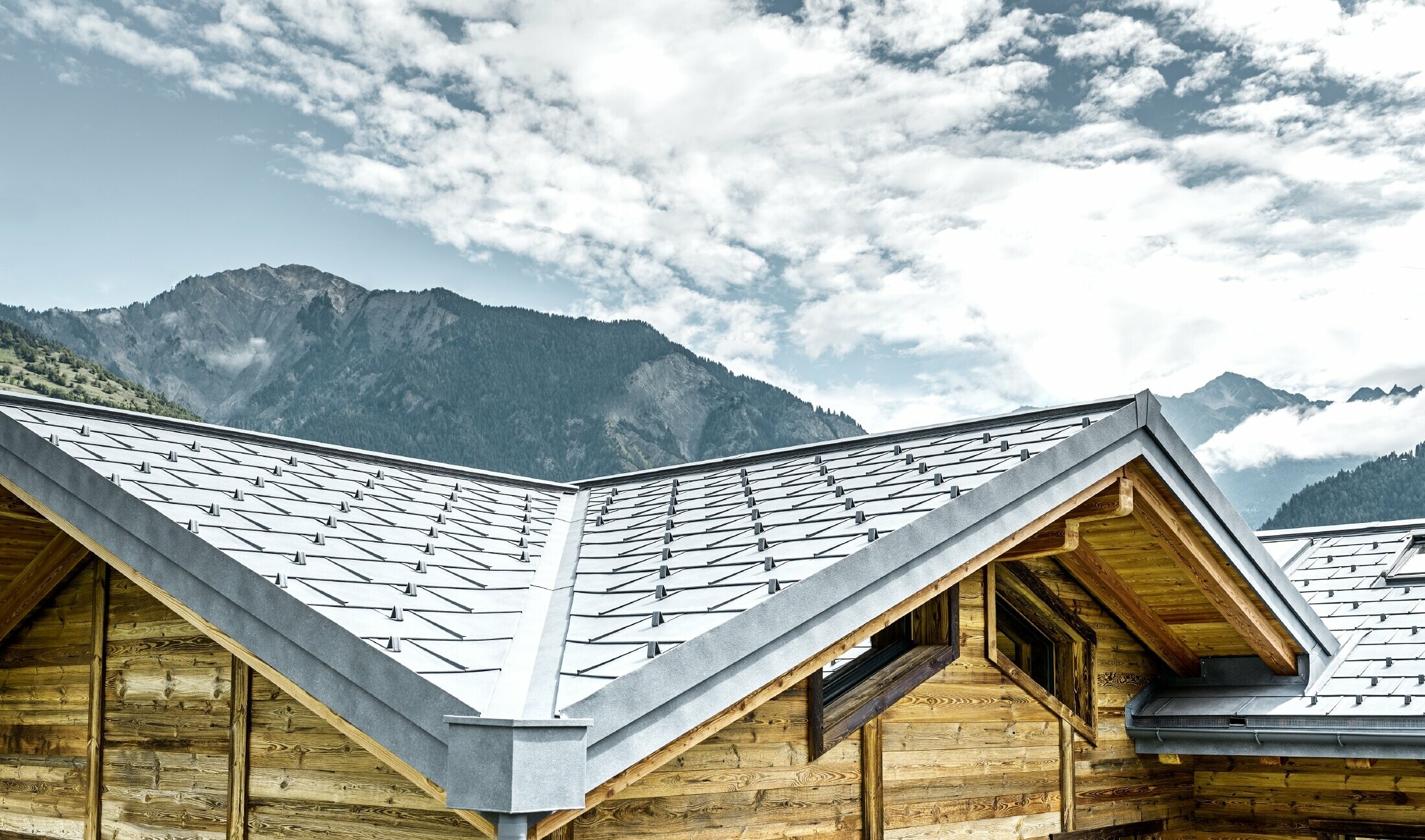 Tetto di un rifugio rustico in Svizzera con facciata in legno e tetto in alluminio di PREFA. La tegola R.16 è stata posata in grigio pietra. Si distinguono il tetto inclinato e la scanalatura.