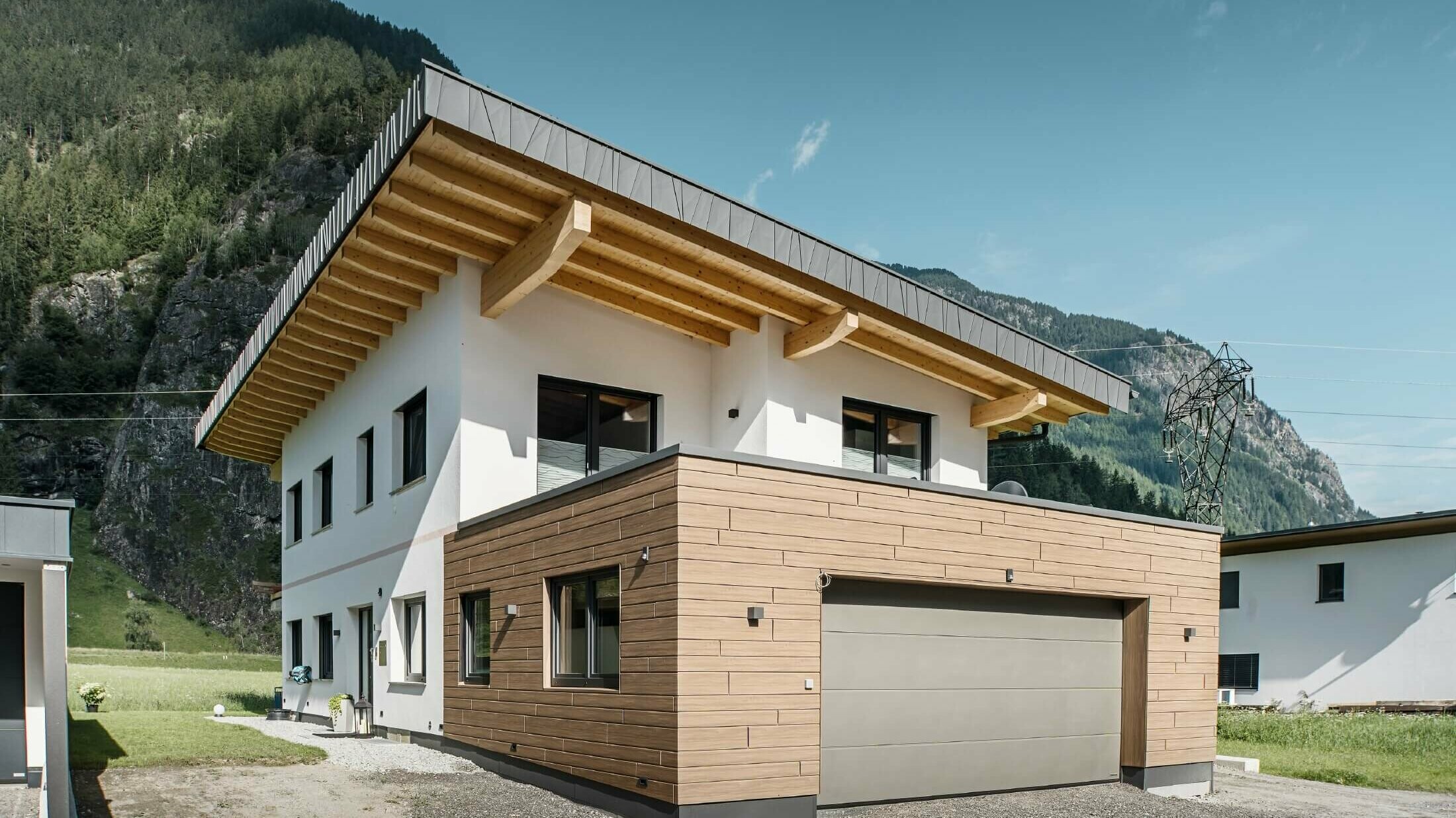 Garage di una palazzina con doghe PREFA effetto legno di colore "noce scuro". Sullo sfondo si vedono le montagne. 