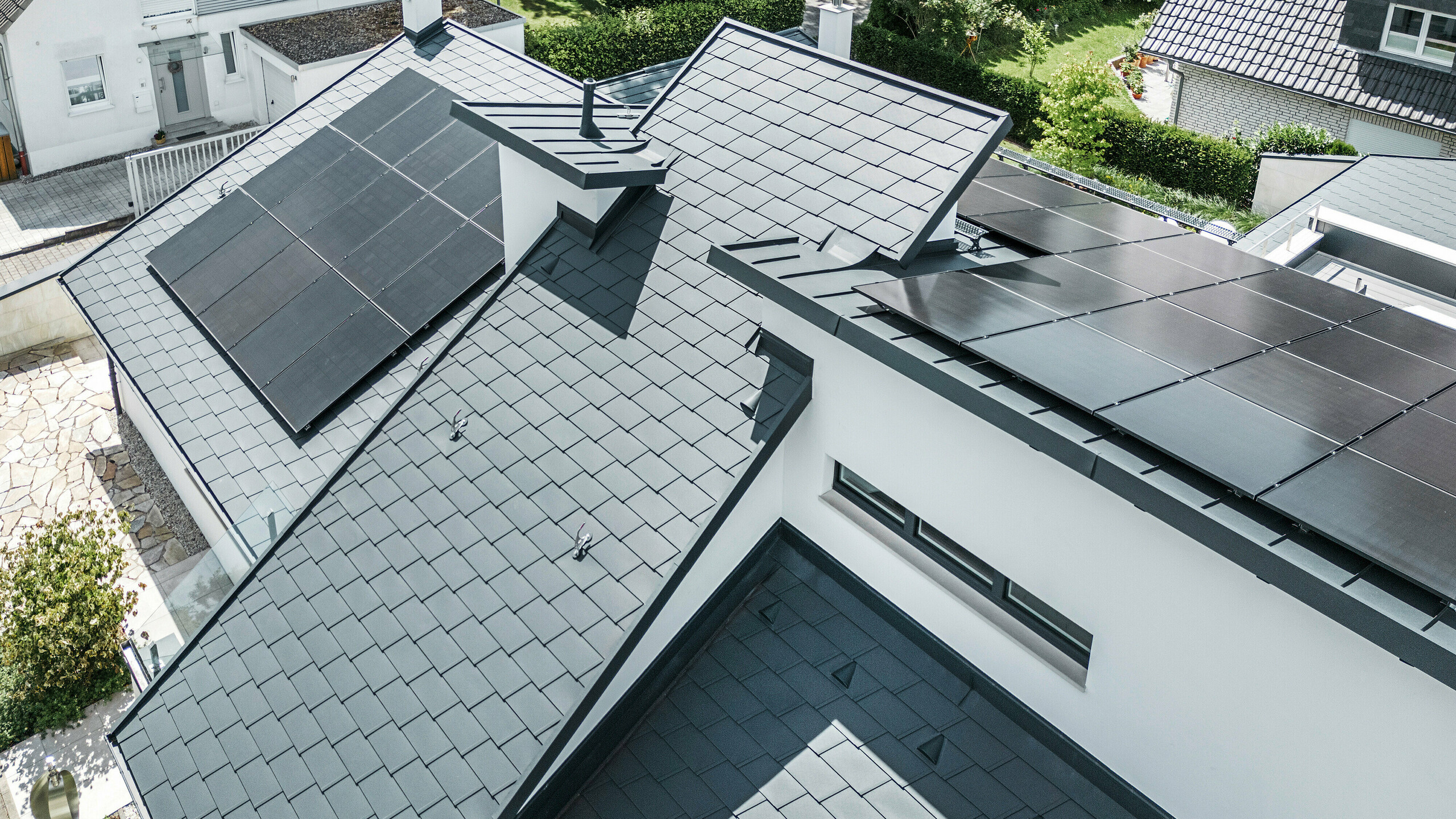 Vista a volo d'uccello dei diversi livelli del tetto di una moderna casa unifamiliare a Dortmund, dotata di PREFA scandola DS.19 e PREFALZ nel colore P.10 antracite e di un impianto fotovoltaico su larga scala.