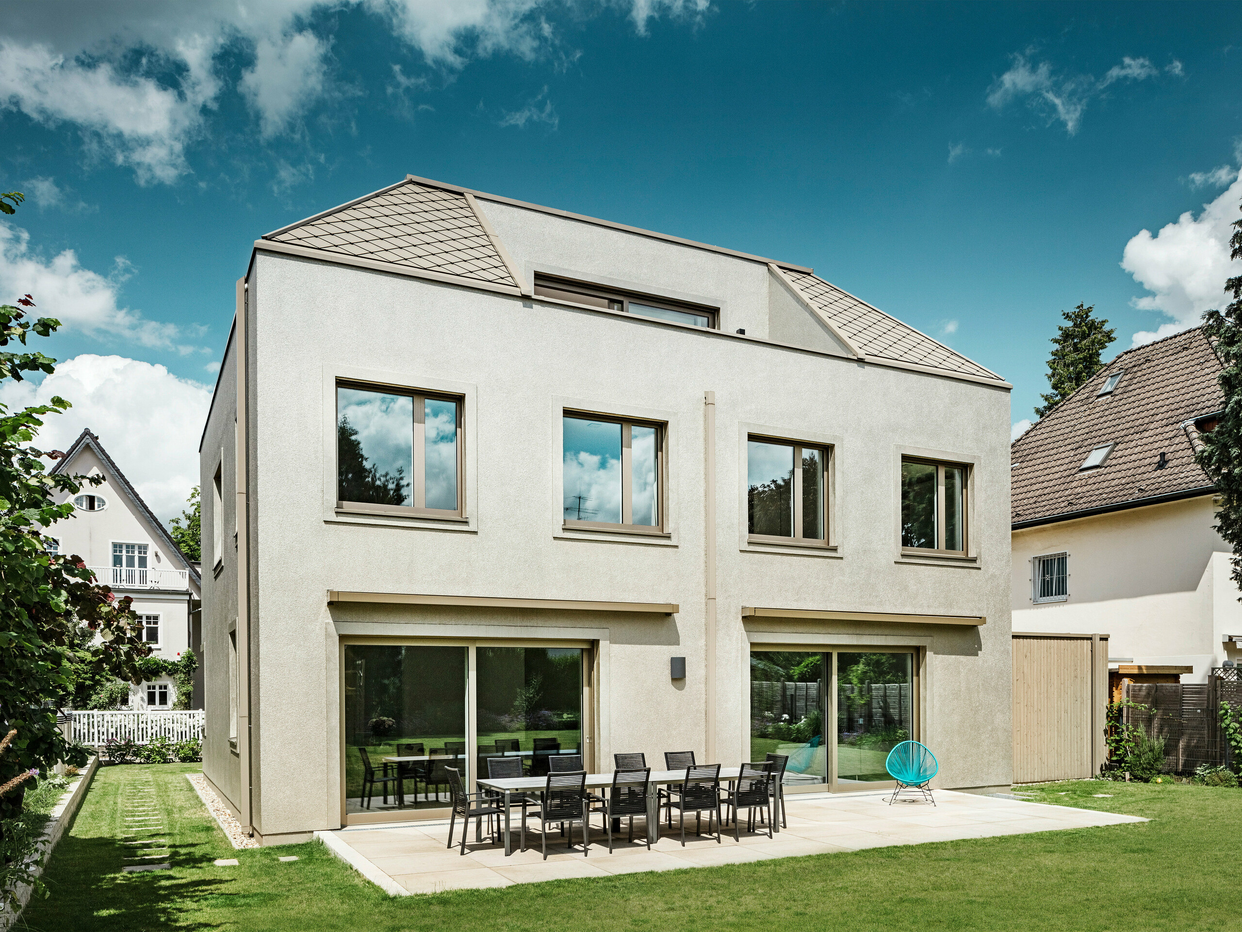 Una moderna casa indipendente con tetto a capanna e rivestimento di facciata e tetto in alluminio color bronzo di PREFA. La casa si trova in un tranquillo quartiere residenziale, circondato da giardini ben curati e da altre case unifamiliari. Sullo sfondo si intravedono grandi finestre che inondano la zona giorno di luce naturale. Una spaziosa terrazza con mobili da giardino invita a rilassarsi e a soffermarsi. Il design della casa si inserisce armoniosamente nell'ambiente circostante, mentre la scelta moderna dei materiali PREFA le conferisce un aspetto contemporaneo ed elegante.