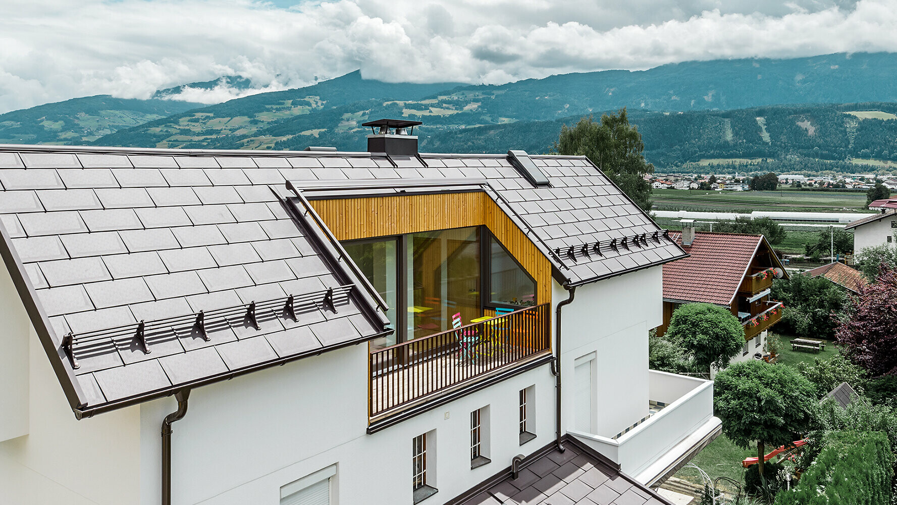 Casa privata rivestita con tegola R.16 in alluminio in testa di moro di PREFA con ampio balcone e facciata intonacata chiara.