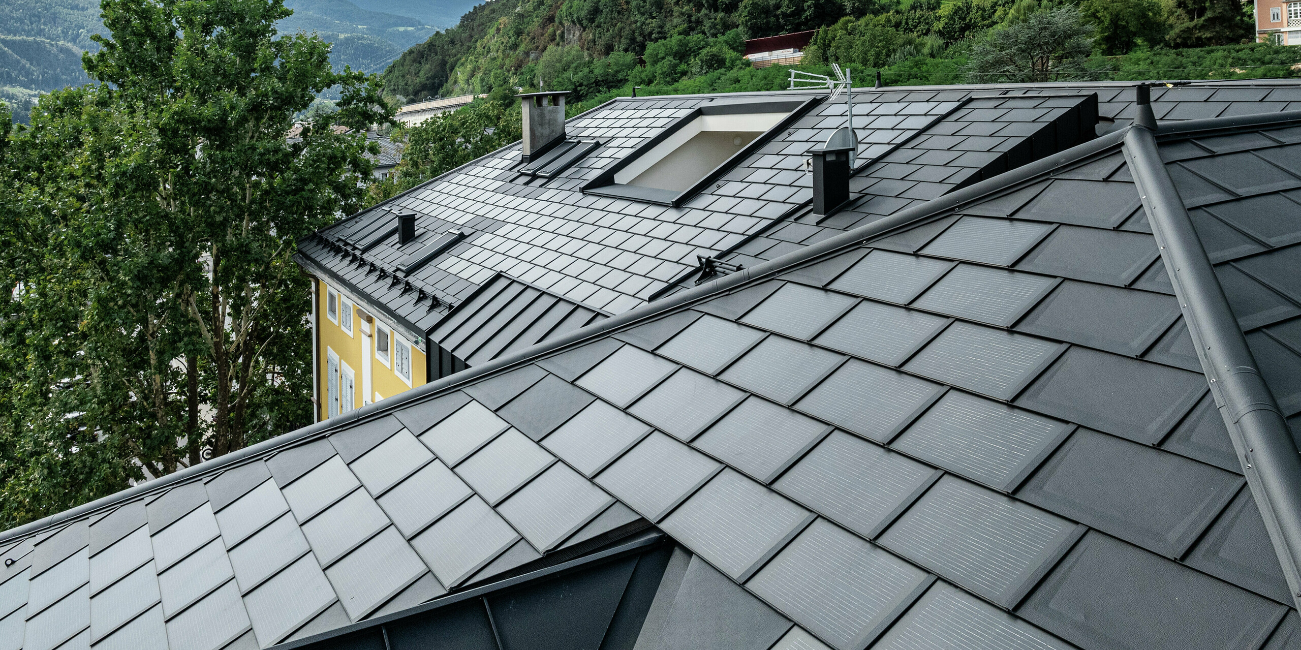 Detailansicht des PREFA Daches am Hotel Jarolim in Brixen mit Solardachplatten, die über integrierte Photovoltaikmodule verfügen, sowie bewährte Dachplatten R.16. Das langlebige Aluminiumdach verbindet innovative Technik mit elegantem Design und ist optimal für denkmalgeschützte Gebäude geeignet. Die Photovoltaikmodule sorgen für eine nachhaltige Energiegewinnung, ohne die ästhetische Harmonie des Daches zu beeinträchtigen. Robustheit, Witterungsbeständigkeit und präzise Verarbeitung unterstreichen die Qualität der PREFA Produkte.