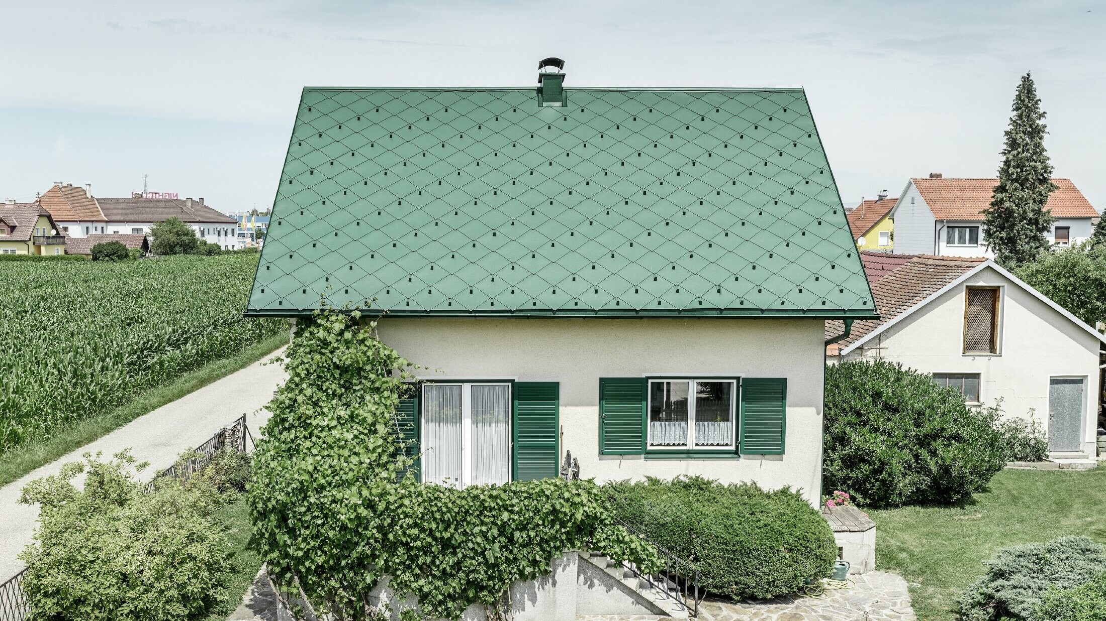 Casa unifamiliare classica con tetto a due falde con copertura in alluminio di colore verde muschio e  persiane verdi. Il tetto è stato coperto con scaglie PREFA 44 × 44 in P.10 verde muschio.