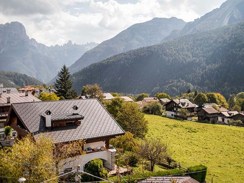 seitlicher Blick auf das traditionelle italienische Haus mit Satteldach und Gaube, verkleidet mir PREFA Dachplatten R.16 in P.10 Nussbraun inklusive Schneehaken