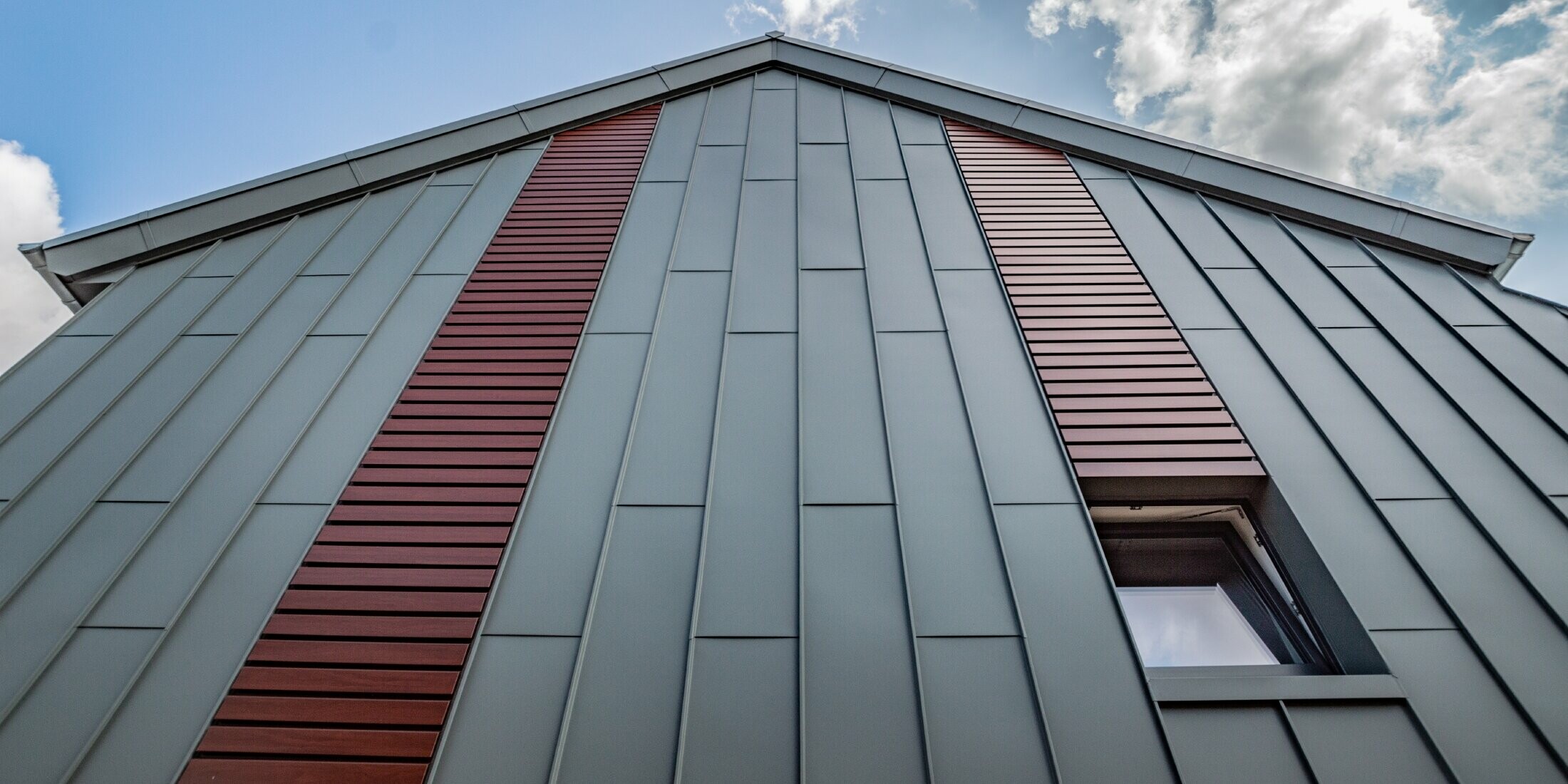 Facciata ad aggraffatura angolare verticale con copertura a lastre in grigio chiaro, con doga orizzontale in legno scuro di PREFA.