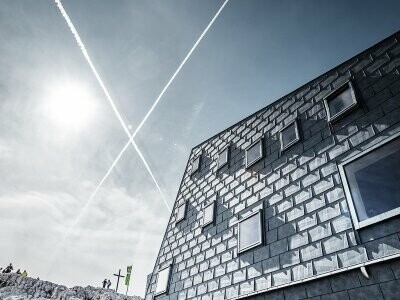 seitliche Ansicht der Seethalerhütte auf 2.740 Metern Höhe vor blauem Himmel, verkleidet mit PREFA Dach- und Fassadenpaneelen FX.12 in P.10 Steingrau