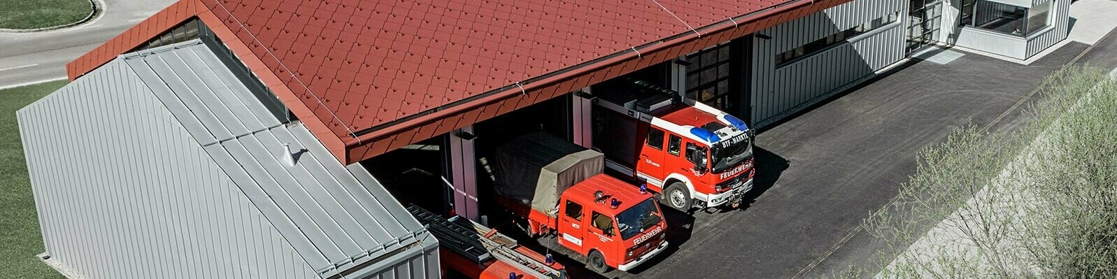 Mezzi dei vigili del fuoco aziendali presso la PREFA. L’edificio presenta un tetto a scaglie di alluminio incombustibile rosse e una facciata in alluminio.