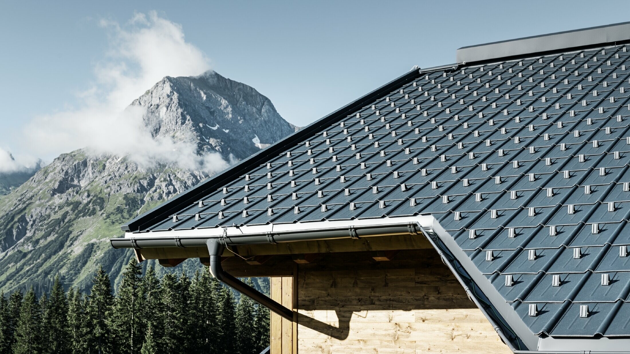 Casa di montagna in legno, il tetto è coperto con tegole PREFA antracite con grondaie PREFA e facciata in legno