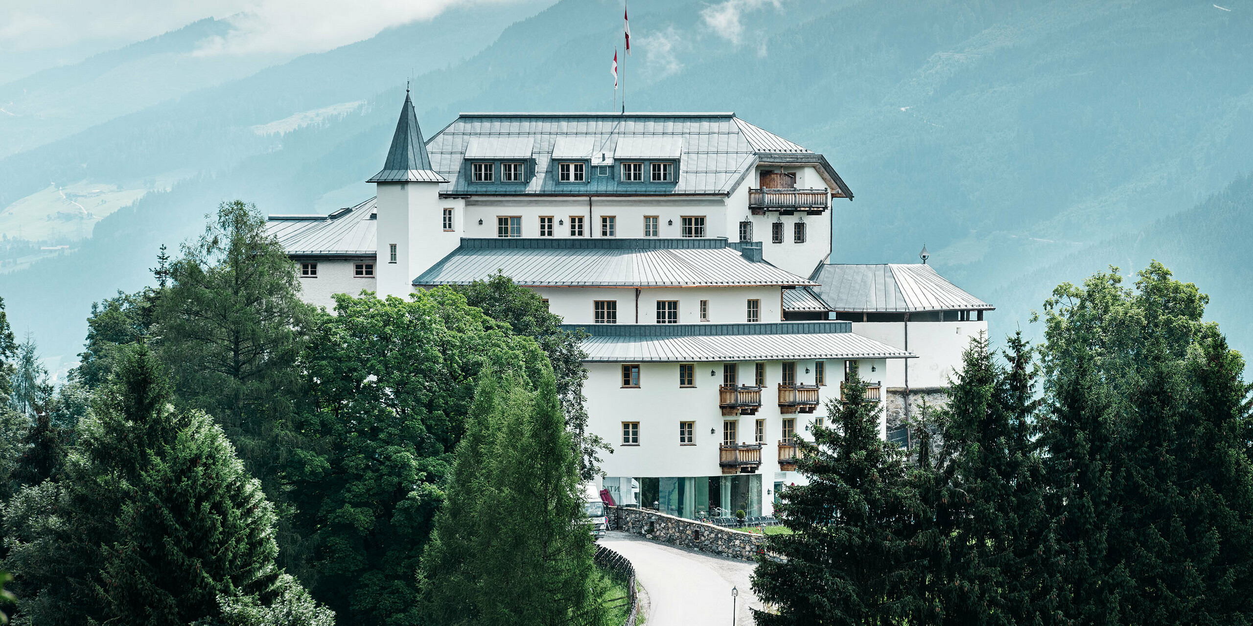 Schloss Mittersill umgeben von Bäumen und Bergen mit einem neu sanierten Prefalz Dach in steingrau