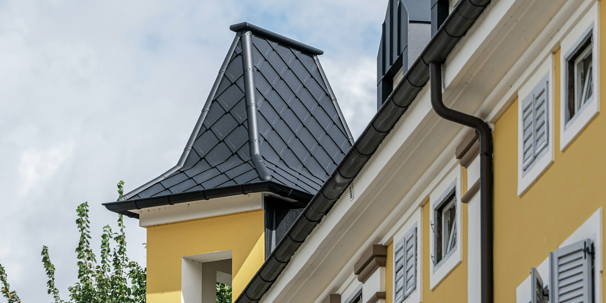 Detailansicht des historischen Turmes des Hotel Jarolim in Brixen, gestaltet mit PREFA Dachrauten aus Aluminium. Die witterungsbeständigen und leichten PREFA Produkte erhalten den historischen Charakter des Gebäudes und sorgen für eine langlebige und ästhetische Dachlösung. Die hochwertige Verarbeitung der Gauben und der Turmverkleidung unterstreicht die Verbindung von traditioneller Architektur und moderner Technik - ideal für denkmalgeschützte Gebäude.