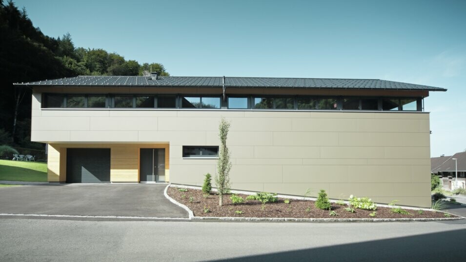 Das Einfamilienhaus in Hohenems präsentiert sich in einer modernen und stilvollen Fassade aus PREFA Aluminium Verbundplatten in Bronzemetallic, mit einem darüberliegenden Dach aus PREFA Dachplatten in P.10 Anthrazit. Die klare Linienführung und das durchdachte Farbkonzept des Designs integrieren das Gebäude nahtlos in die natürliche Umgebung. Die Gestaltung zeigt die Kombination aus Funktionalität und Ästhetik, die PREFA Produkte für zeitgemäße Wohnarchitektur bieten.