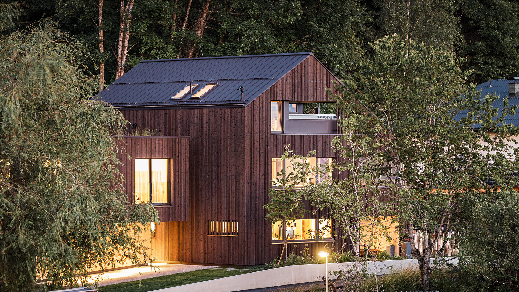 Ripresa notturna della casa plurifamiliare illuminata in un ambiente naturale da una prospettiva laterale.