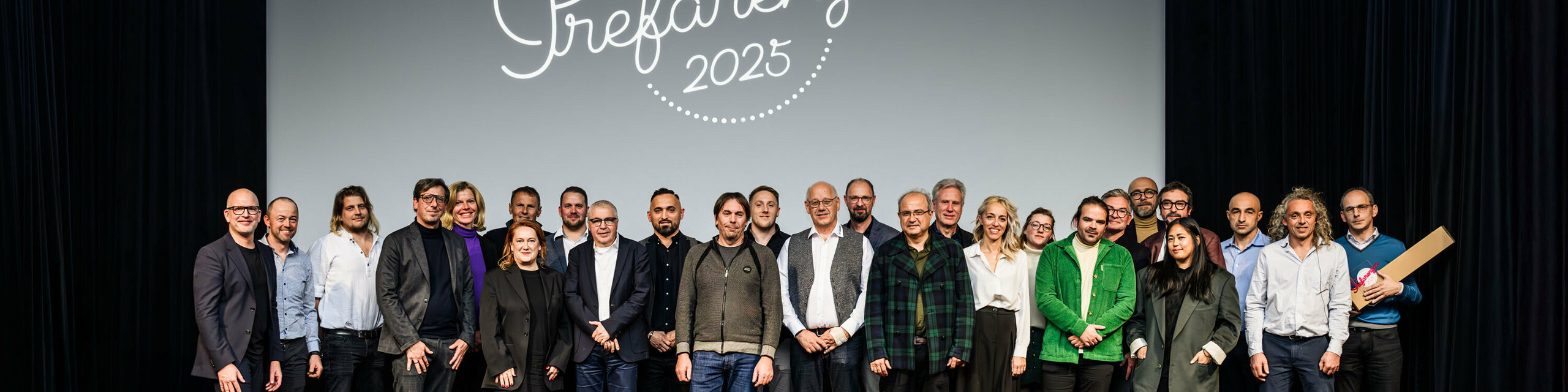 Gruppenfoto bei der PREFARENZEN-Premiere 2025 im Stadtkino Wien: Jürgen Jungmair, Marketingleiter von PREFA, mit den Mitwirkenden und Gästen vor dem Logo der Veranstaltung ‚Prefarenzen 2025‘ auf der Leinwand. Die Teilnehmer:innen repräsentieren Architektur, Planung, Verarbeitung und Medien aus ganz Europa.