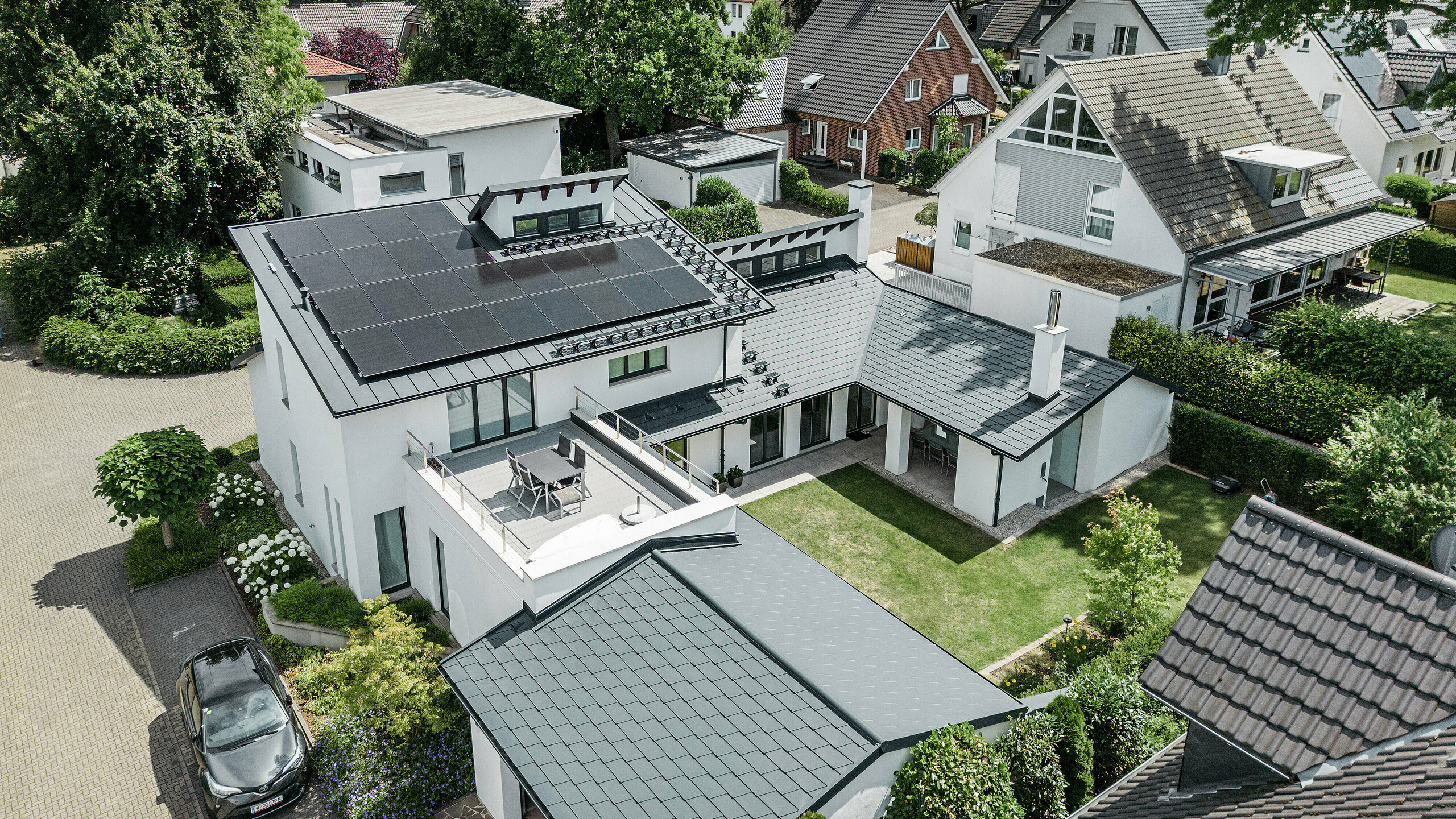 Vista a volo d'uccello dell'eccezionale paesaggio del tetto di una casa unifamiliare a Dortmund con scandola DS.19 PREFA e PREFALZ in P.10 antracite e un impianto fotovoltaico di grandi dimensioni.