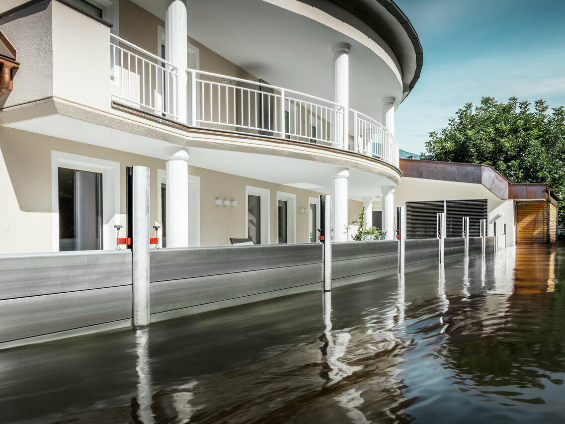 L'immagine mostra una casa indipendente con balcone. Il sistema anti-esondazione PREFA protegge la casa dall'innalzamento delle acque di piena.