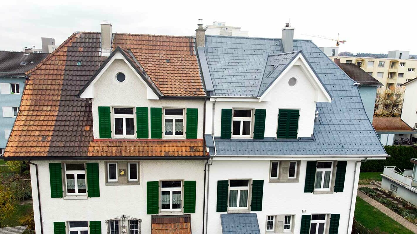 Metà di una casa bifamiliare in Svizzera; la parte sinistra dell’edificio non è ancora stata ristrutturata e presenta ancora una copertura in vecchio laterizio. La copertura della parte destra dell’edificio è stata realizzata con pannelli PREFA grigio pietra.